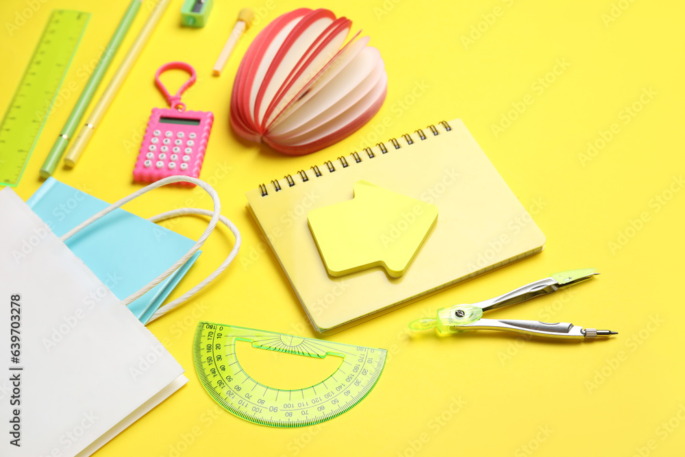 Composition with paper bag and different stationery on yellow background, closeup