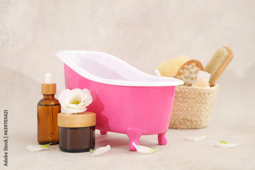 Composition with small bathtub, bath supplies and flower petals on light background