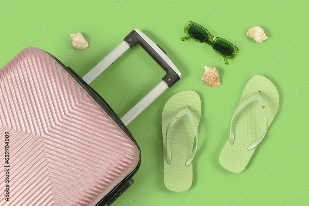 Suitcase, sunglasses, flip-flops and seashells on color background