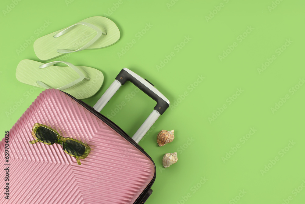 Suitcase, sunglasses, flip-flops and seashells on color background