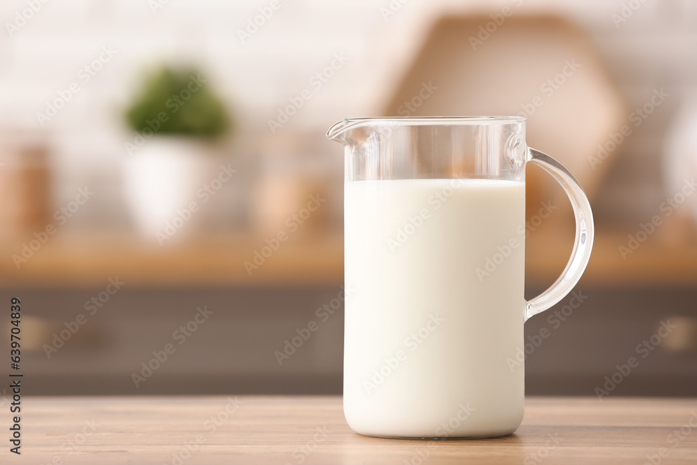 Jug of fresh milk on wooden table in kitchen