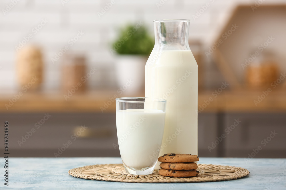 Glass and bottle of fresh milk with sweet cookies on blue table in kitchen