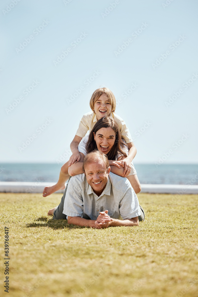 Portrait, grass and family in a pile by the ocean together for travel, vacation or holiday on a summ