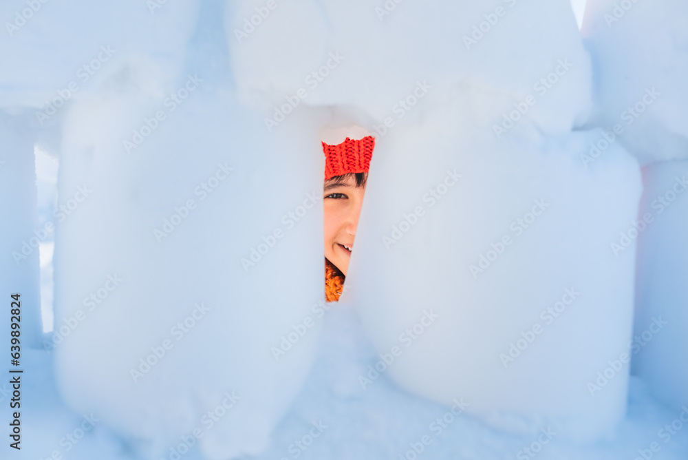 Little boy is playing in snow house. Child is peering into crack in the wall. Active winter outdoor 