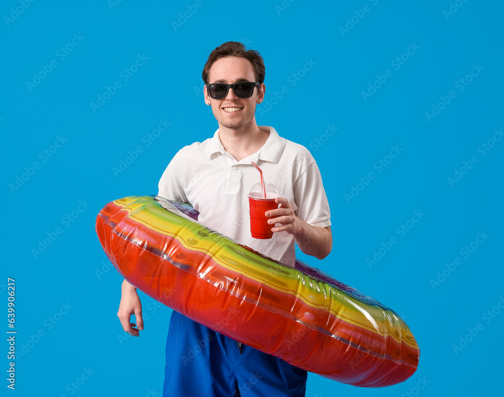 Young man with inflatable ring and cup of soda on blue background