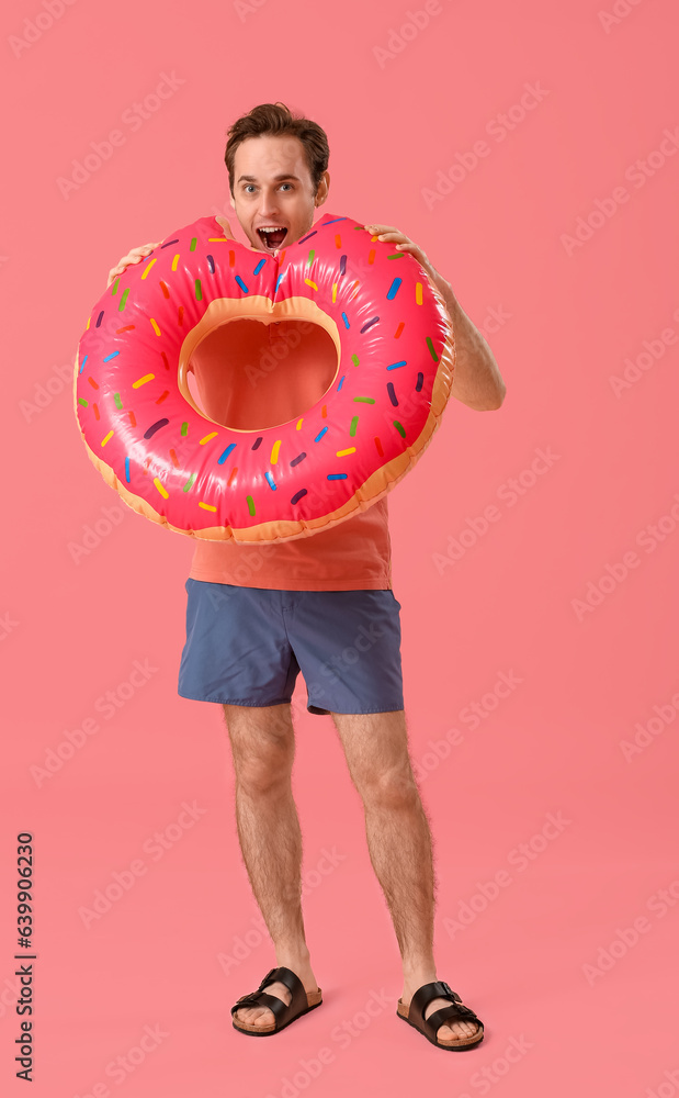 Young man with inflatable ring on pink background