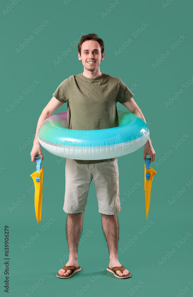 Young man with inflatable ring and flippers on green background