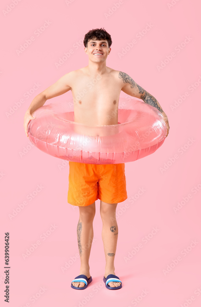 Young man with inflatable ring on pink background