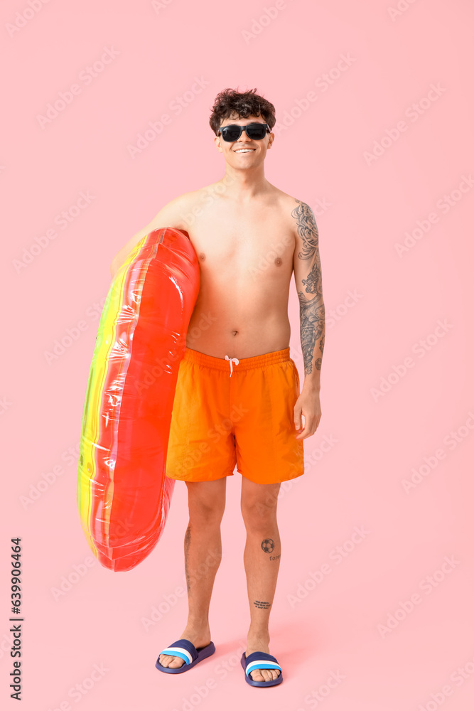 Young man with inflatable ring on pink background