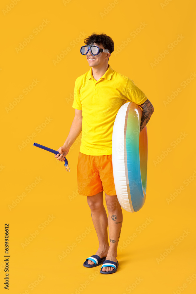 Young man in snorkeling mask with inflatable ring on yellow background