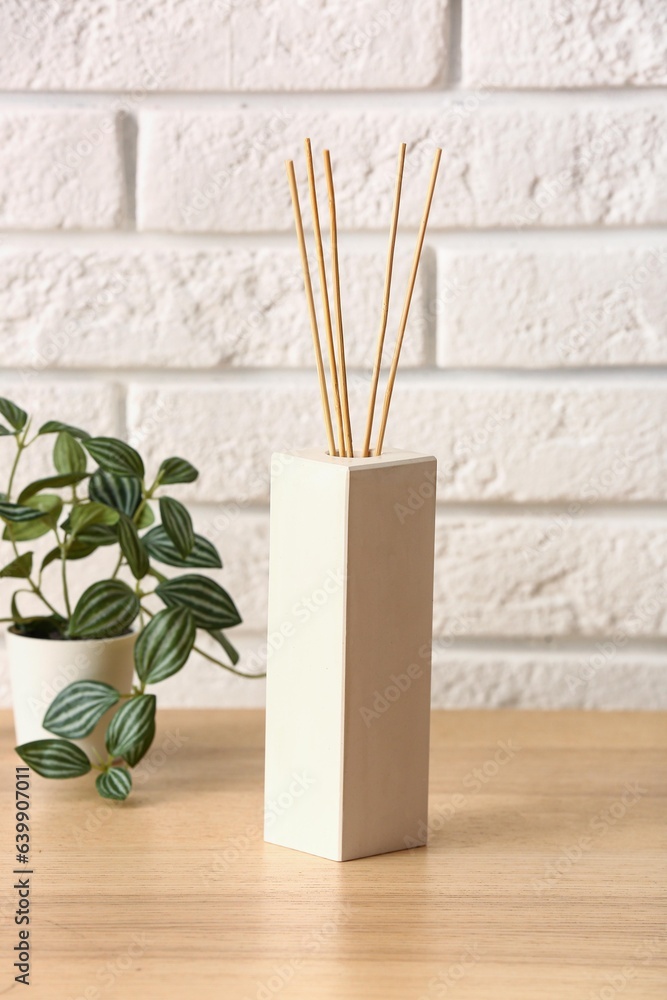 Bottle of reed diffuser and houseplant on table near light brick wall in room, closeup