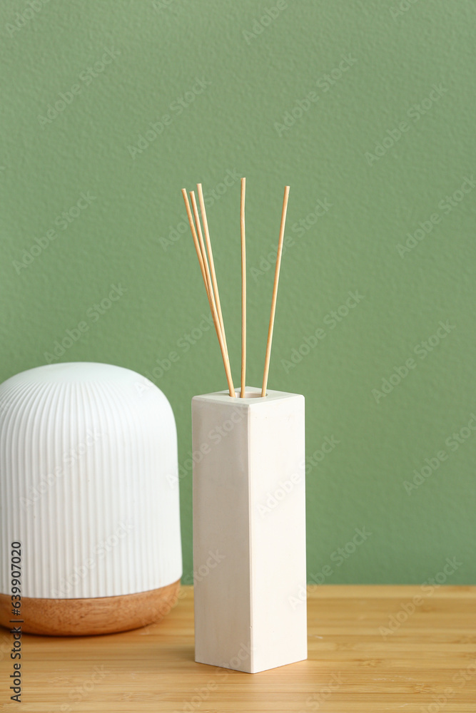 Bottle of reed diffuser on table near color wall in room, closeup