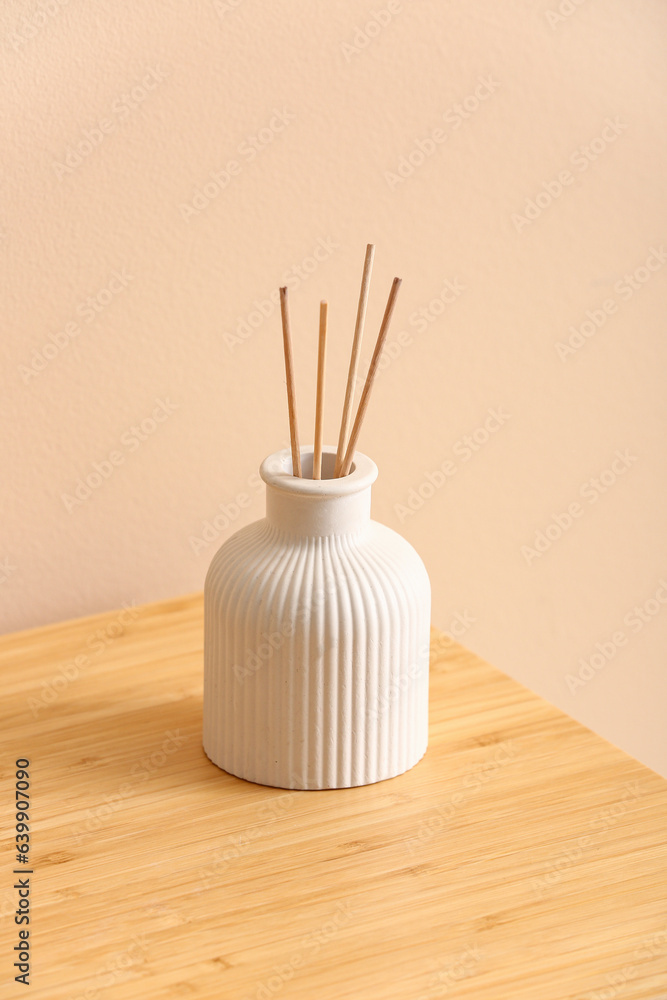 Bottle of reed diffuser on table near beige wall in room