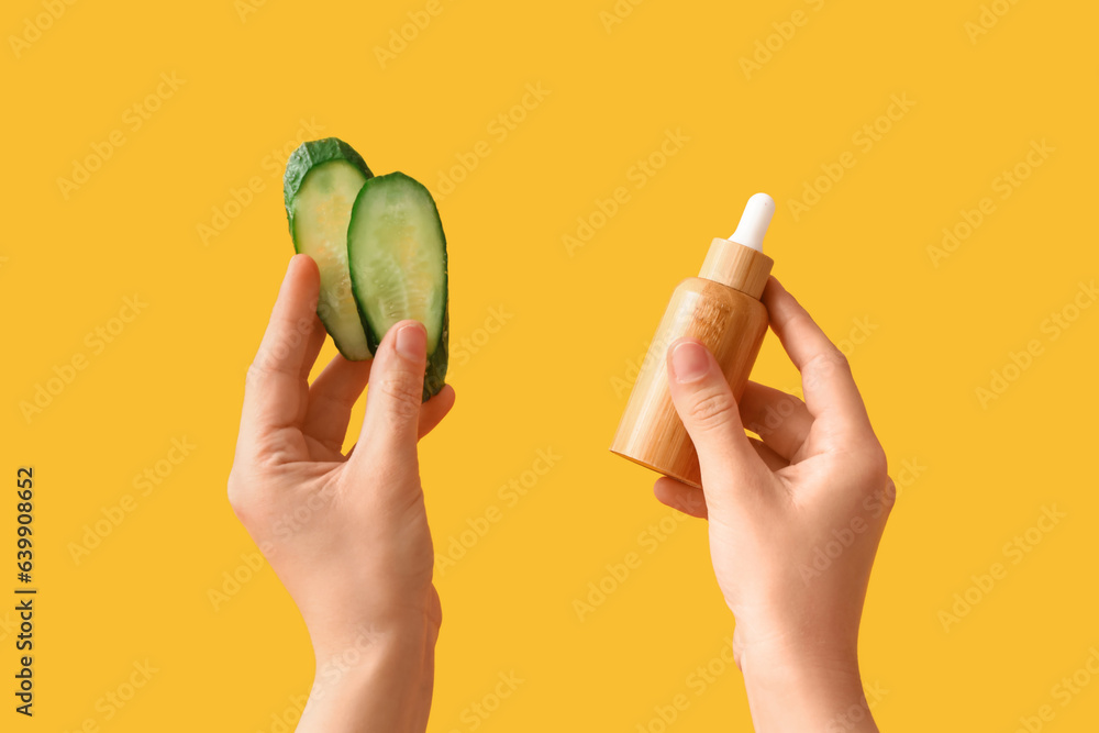 Woman with cosmetic dropper bottle and cucumber slices on yellow background