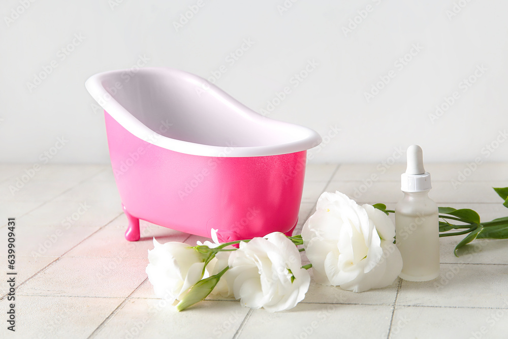 Composition with small bathtub, bottle of essential oil and eustoma flowers on light tile table