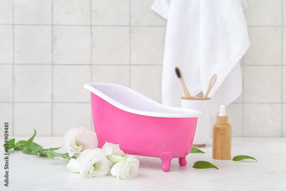 Small bathtub, eustoma flowers and bath supplies on light table