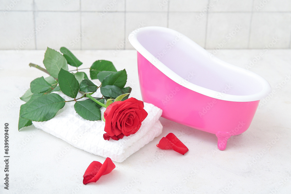 Small bathtub, rose flower and clean towel on light table