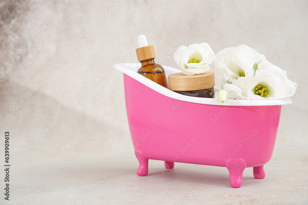 Small bathtub with cosmetic products and eustoma flowers on light background