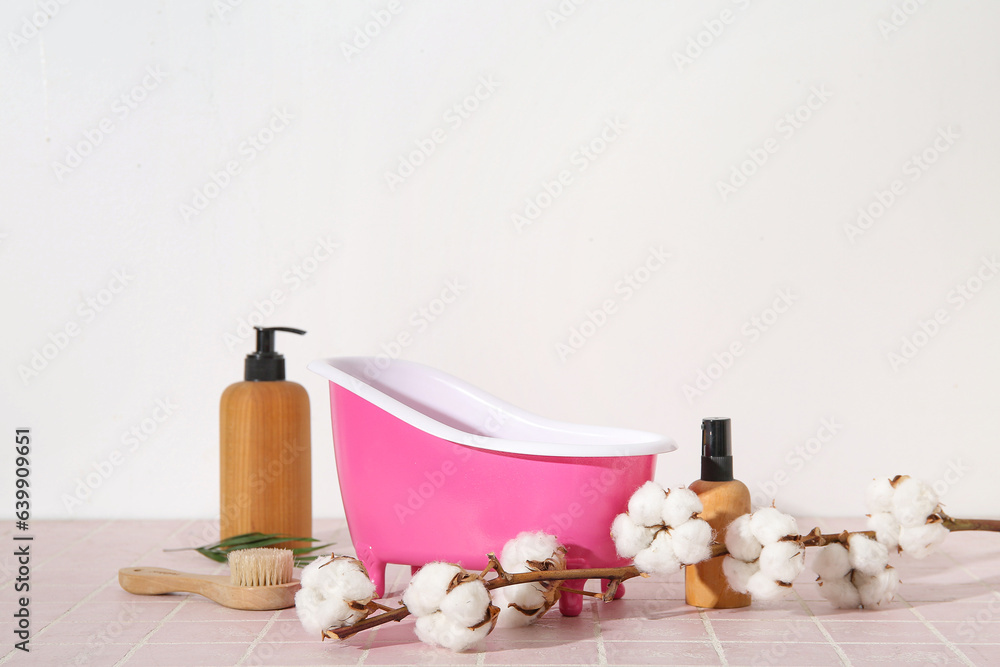 Composition with small bathtub, bath supplies and cotton branch on color tile table