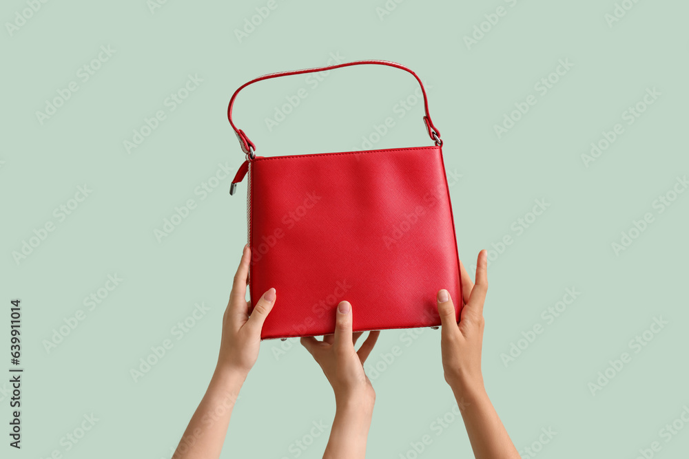 Female hands holding stylish bag on pale green background