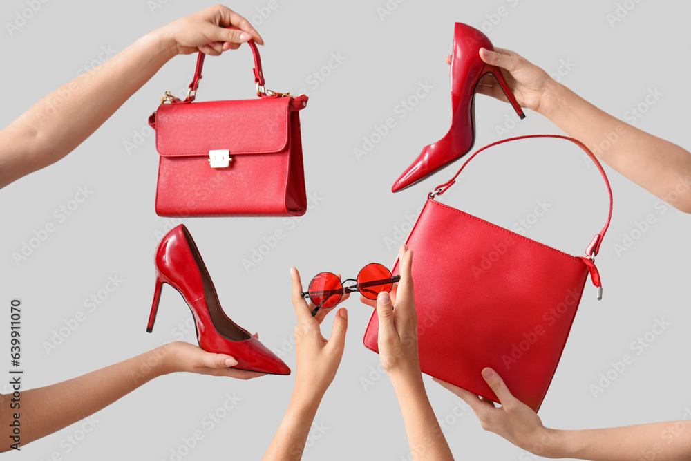 Female hands holding different stylish bags, sunglasses and high heels on grey background