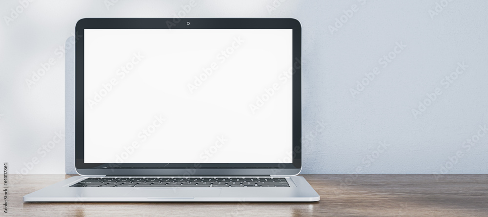 Wide image of laptop with empty white mock up screen placed on wooden desk. Concrete wall with shado