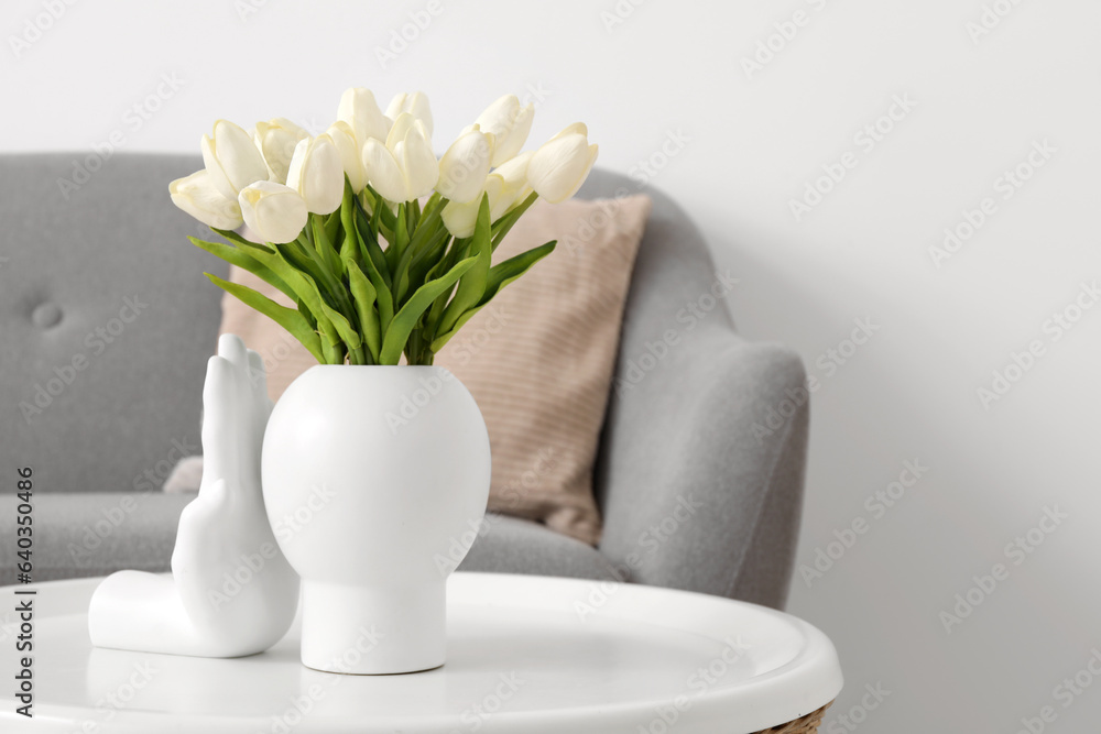 Vase with beautiful tulip flowers on table near grey sofa