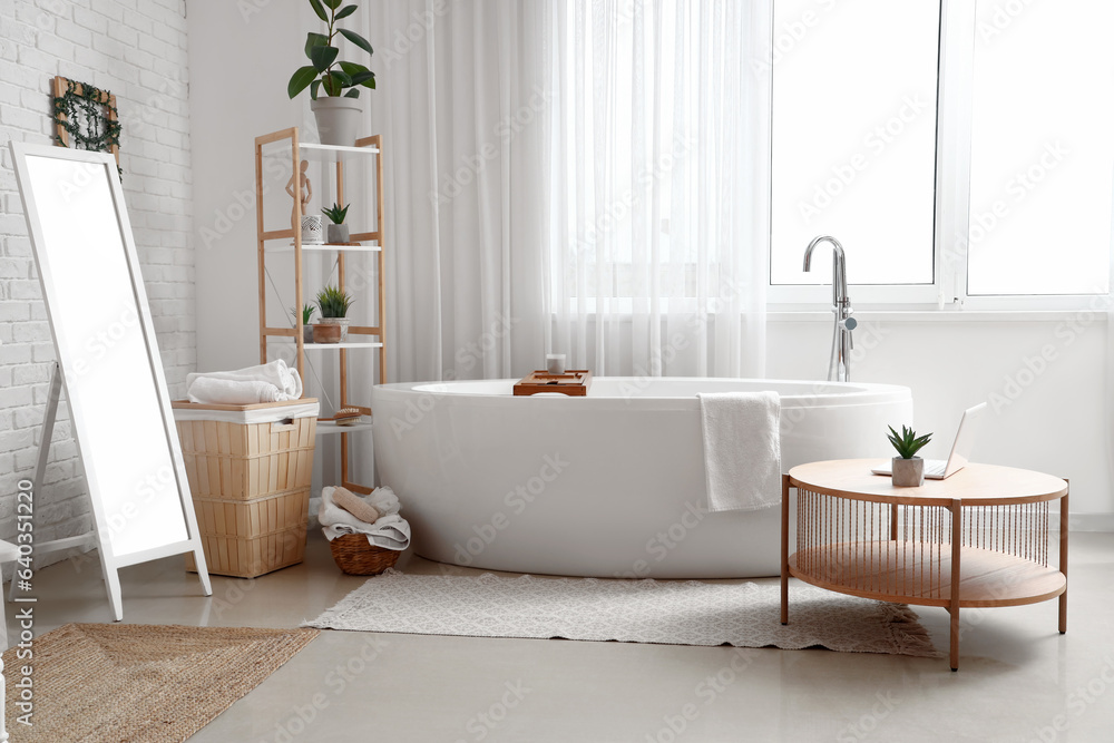 Interior of light bathroom with bathtub, mirror and coffee table