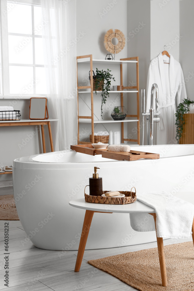 Interior of light bathroom with bathtub and bathing supplies on table