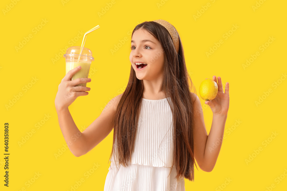 Little girl with glass of smoothie and lemon on yellow background