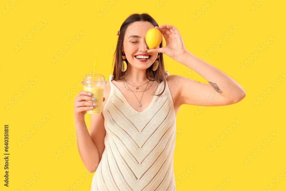 Young woman with glass of smoothie and lemon on yellow background