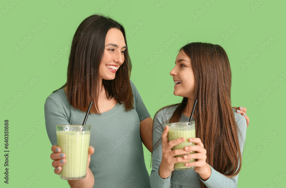 Little girl with her mother drinking smoothie on green background