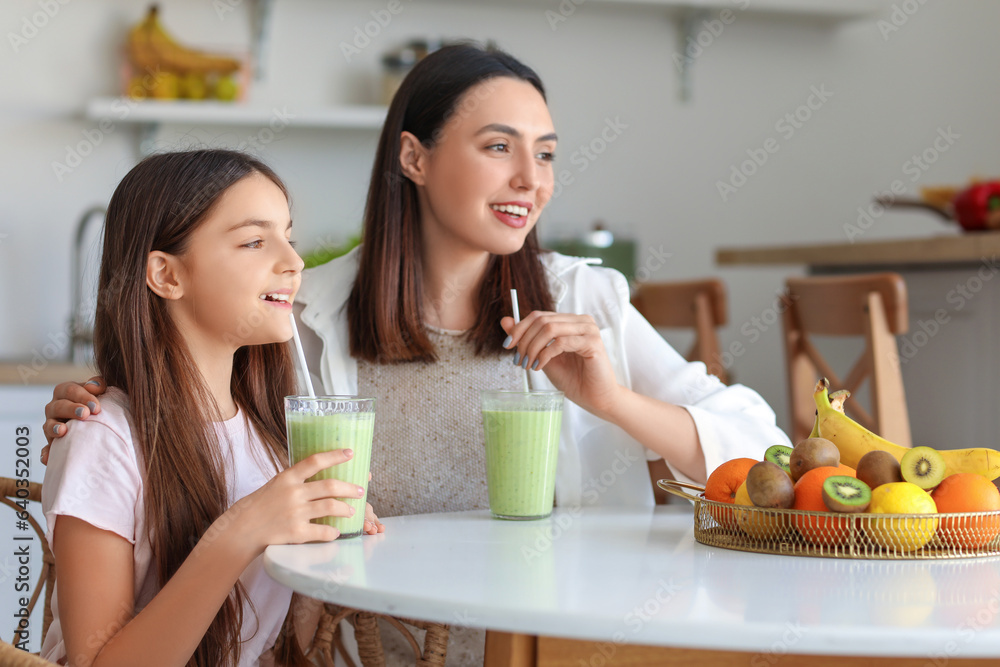 Little girl with her mother drinking green smoothie at table in kitchen