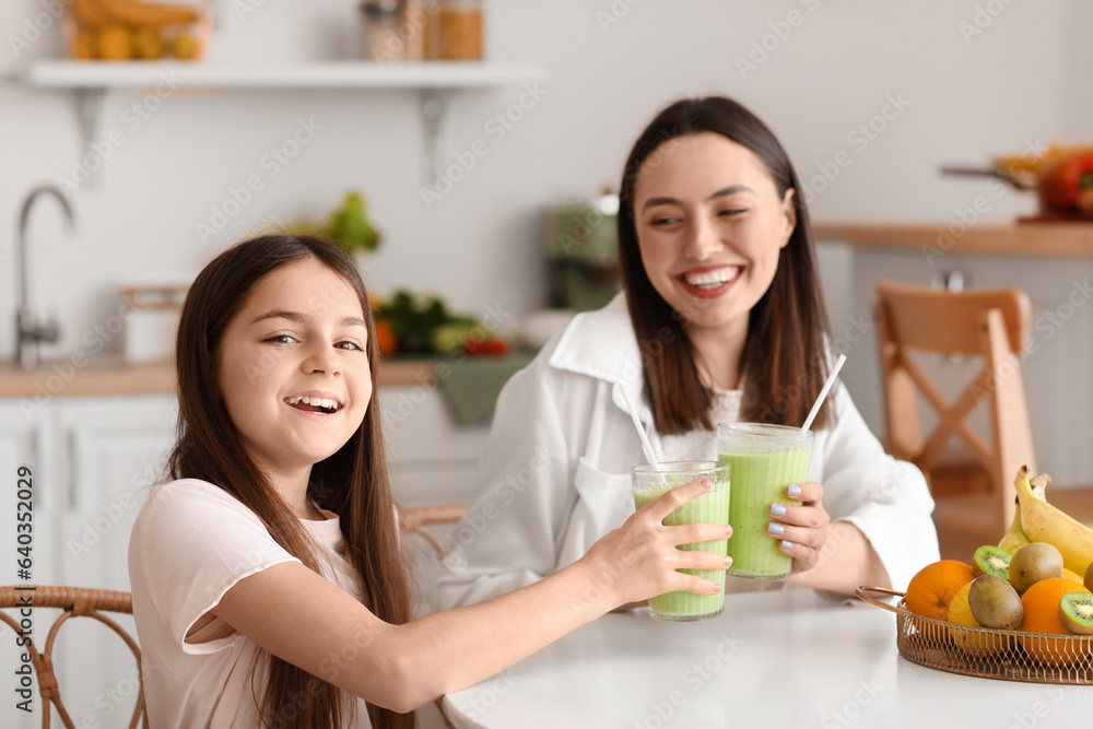 Little girl with her mother drinking green smoothie at table in kitchen