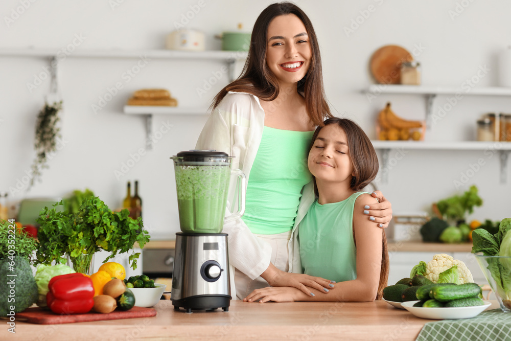 Little girl and her mother making vegetable smoothie with blender in kitchen