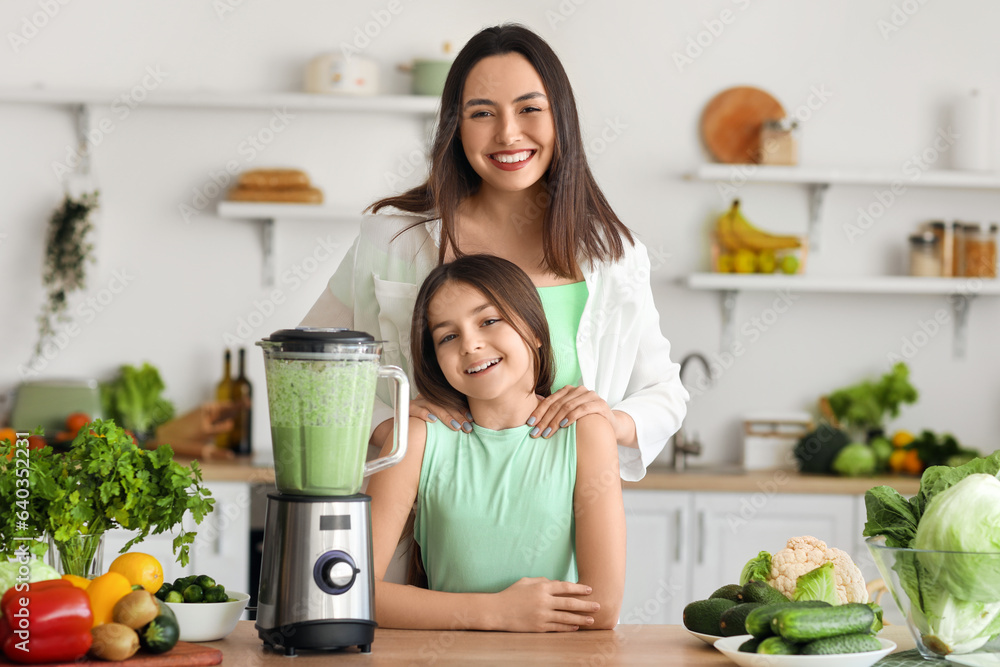 Little girl and her mother making vegetable smoothie with blender in kitchen