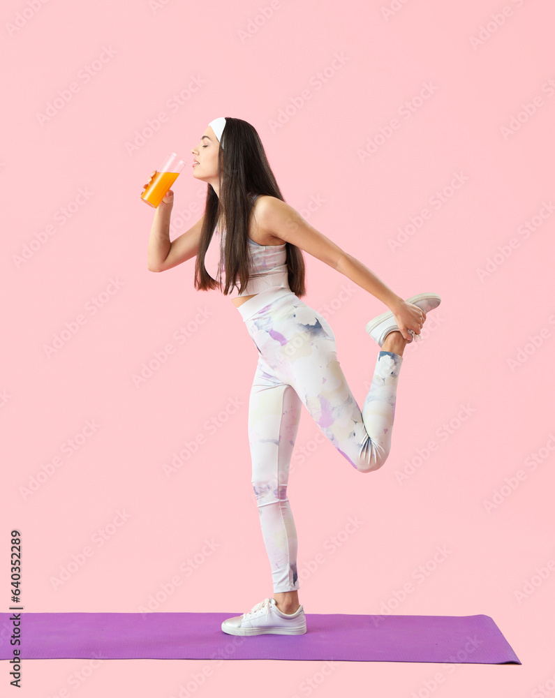 Sporty young woman with glass of vegetable juice training on pink background