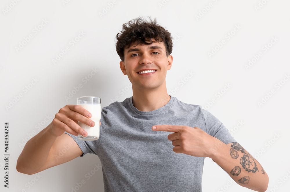 Young man pointing at glass of milk on white background