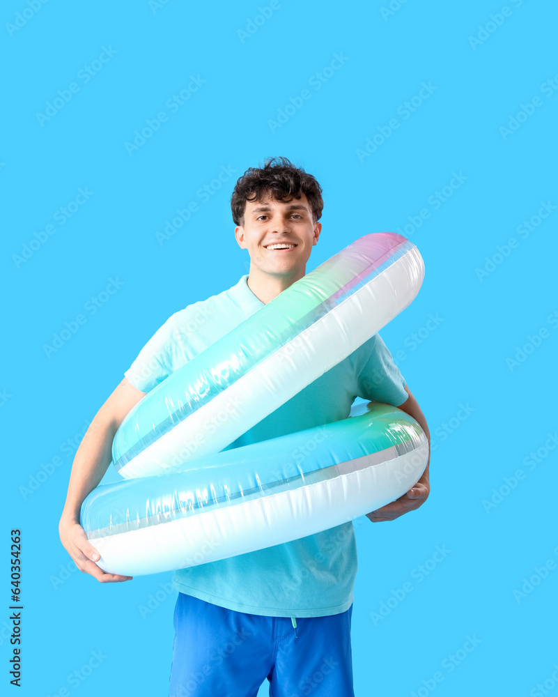 Young man with inflatable rings on blue background