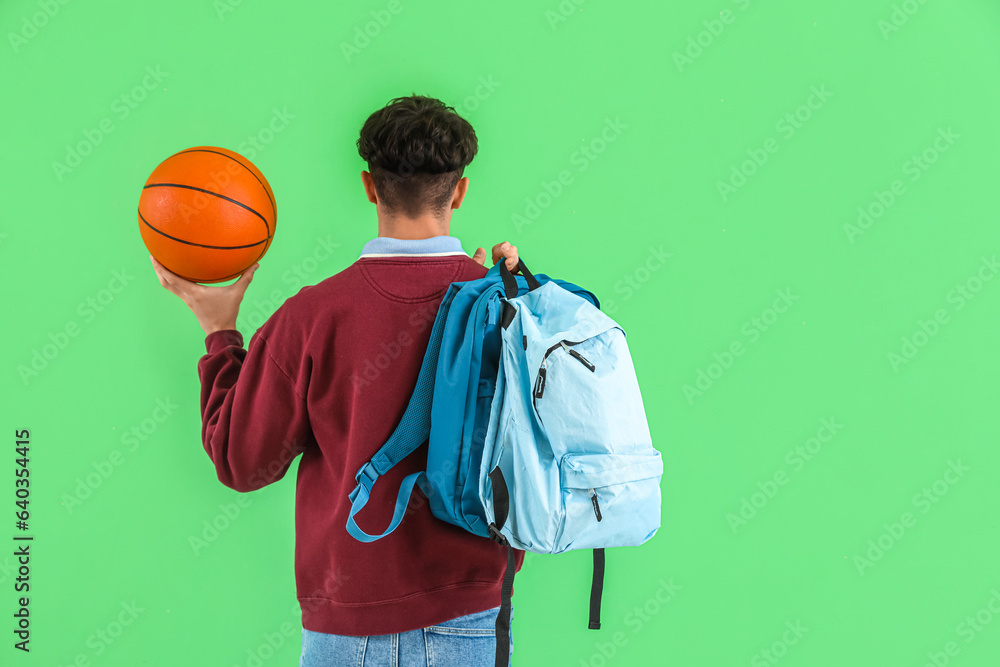 Male student with ball and backpacks on green background, back view