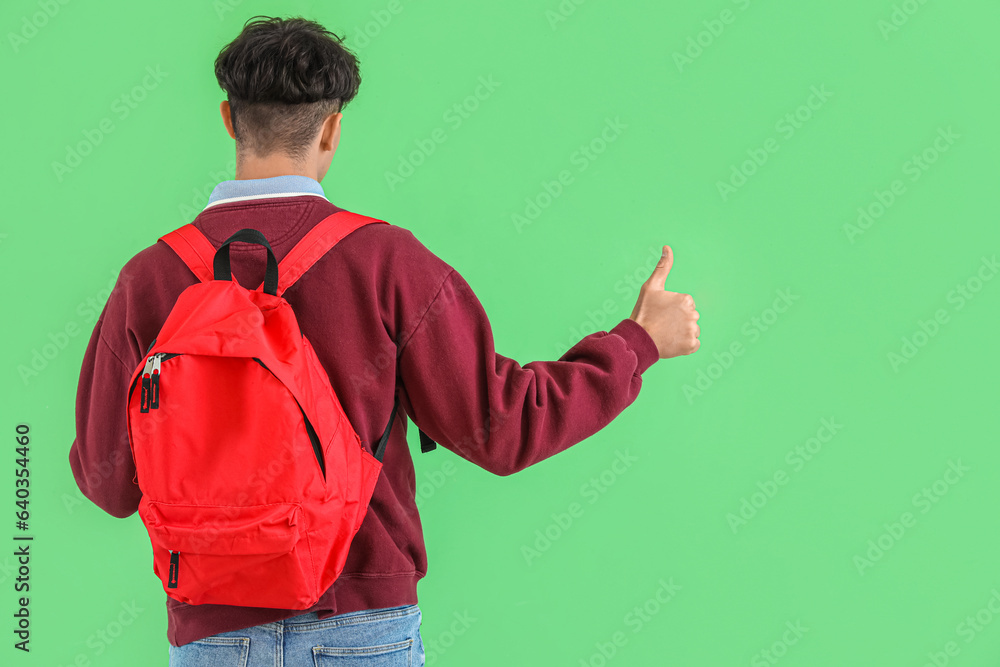 Male student with backpack showing thumb-up on green background, back view