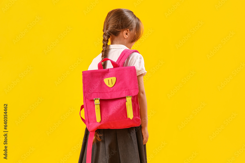 Little schoolgirl with backpack on yellow background, back view