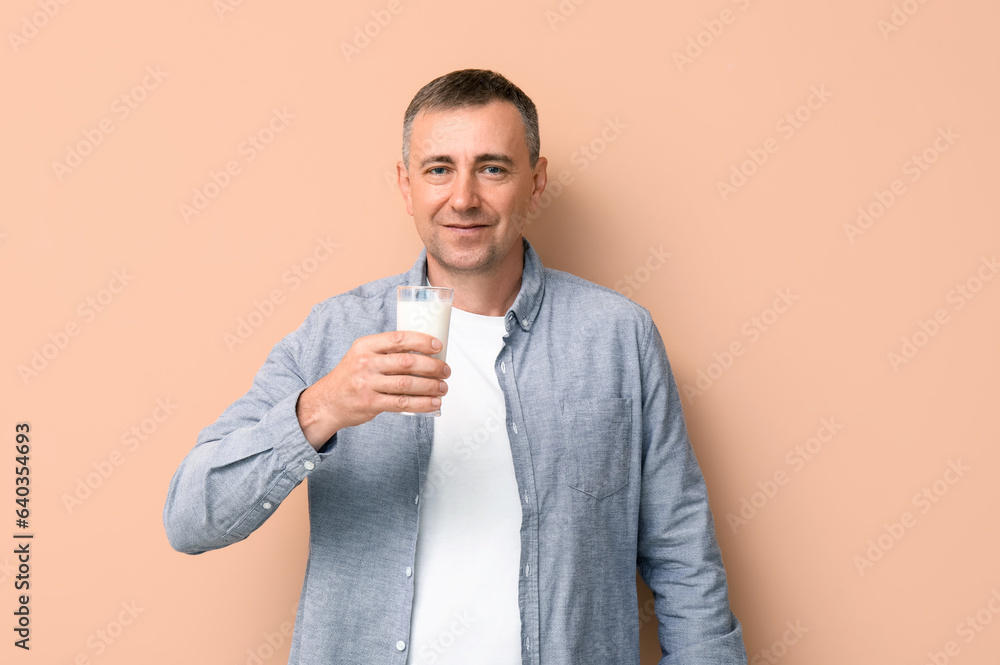 Mature man with glass of milk on beige background