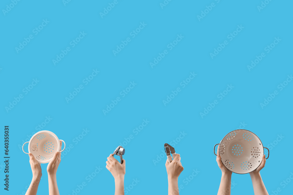 Female hands holding colanders, sieves and kitchen utensils on blue background