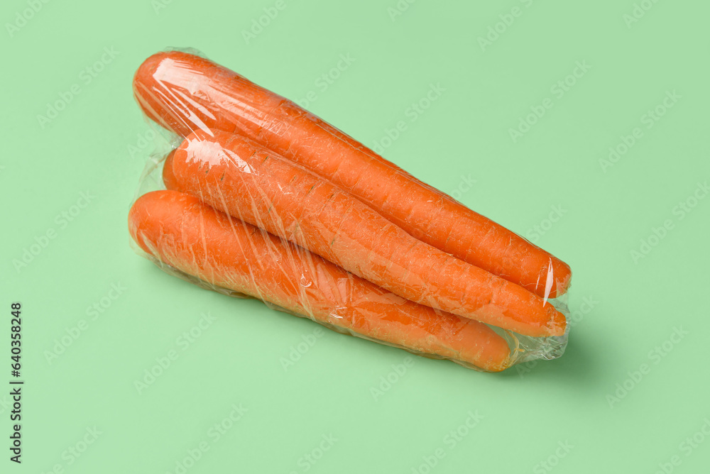 Fresh carrot wrapped in stretch wrap on color background