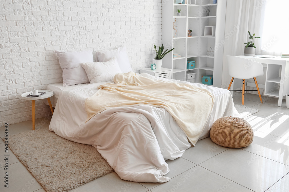 Interior of light childrens bedroom with cozy bed, shelving unit and desk near window