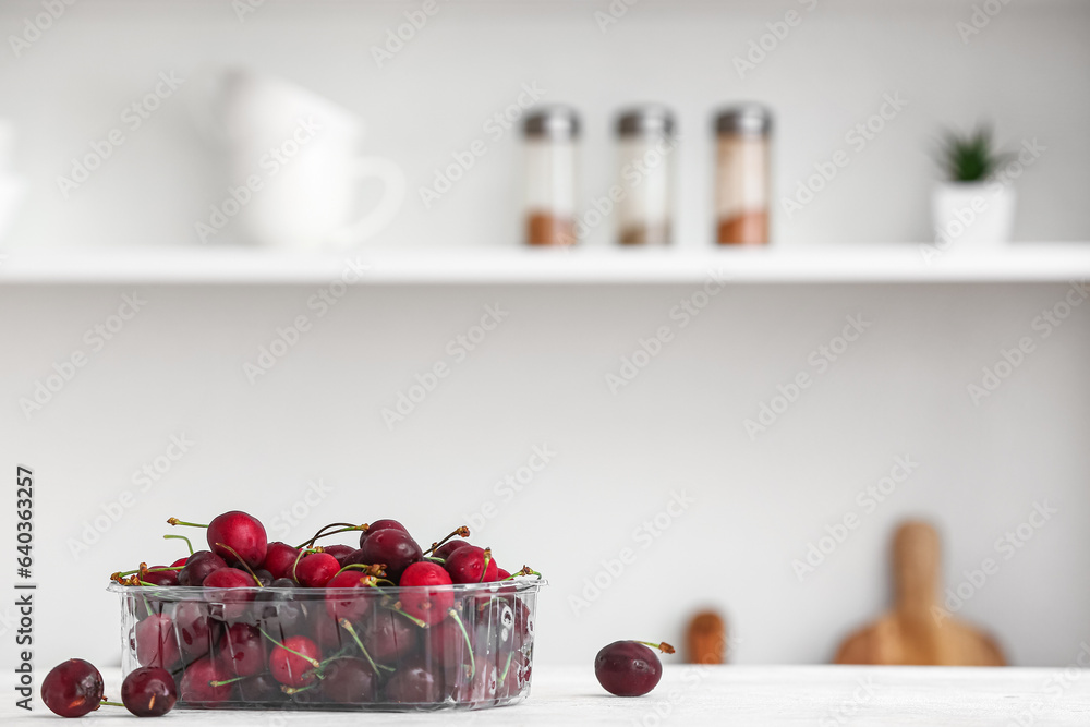 Plastic container with ripe cherries on table in kitchen