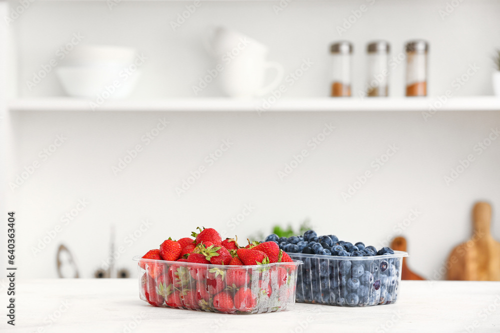 Plastic containers with ripe berries on table in kitchen