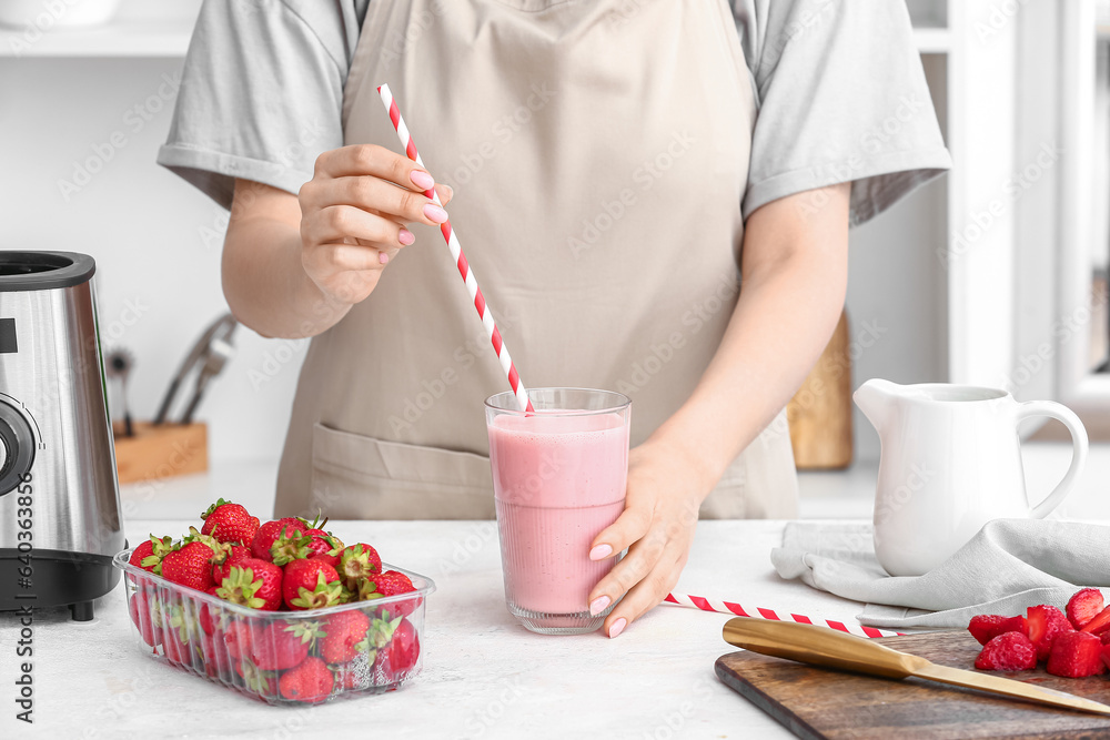 Woman with glass of tasty strawberry smoothie at table in kitchen