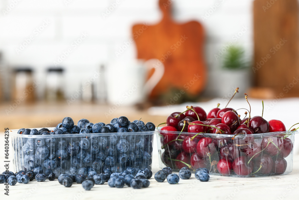 Plastic containers with fresh berries on table in kitchen